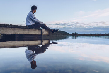 Junger Mann sitzt am Inari-See und schaut auf die Aussicht, Finnland - RSGF00095