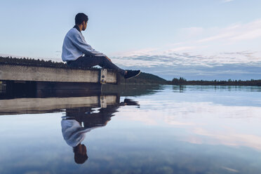 Young man sitting at lake Inari, looking at view, Finland - RSGF00095