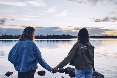 Freundinnen mit Blick auf den Inari-See, Finnland, halten sich an den Händen - RSGF00098