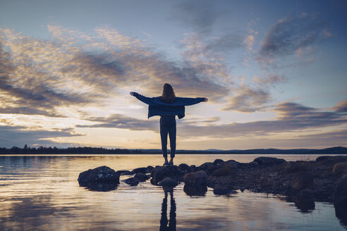 Young woman standing at lake Inari, with arms outstretched, Finland - RSGF00100