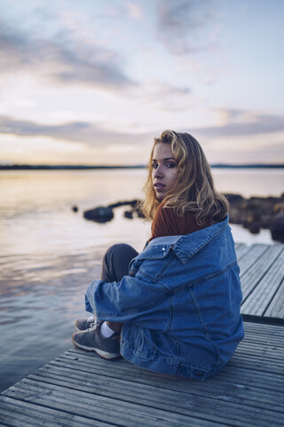 Junge Frau sitzt am Inari-See und schaut in die Kamera, Finnland, lizenzfreies Stockfoto