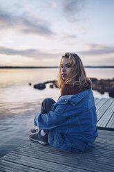 Young woman sitting at lake Inari, looking at camera, Finland - RSGF00101