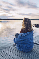 Young woman sitting at lake Inari, looking at view, Finland - RSGF00102