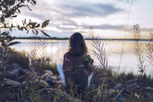 Young woman sitting at lake Inari, looking at view, Finland - RSGF00105