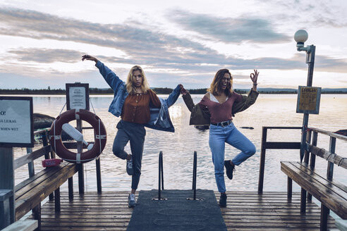 Zwei Freundinnen stehen auf einem Bein auf einem Steg am INari-See, Finnland - RSGF00107