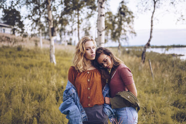 Two girl friends leaning on each other on a lakeshore - RSGF00112