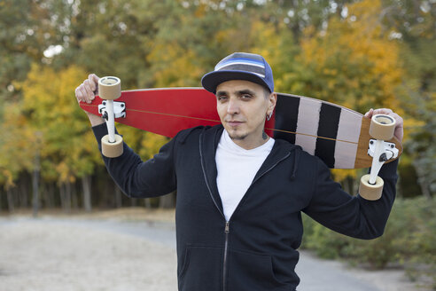 Porträt eines Mannes mit Skateboard auf den Schultern im Herbst - VGF00099