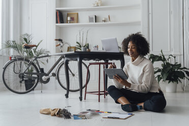 Disigner sitting on ground of her home office, using digital tablet - BOYF00913