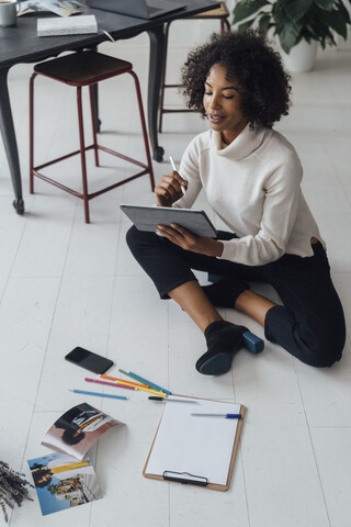 Disigner sitting on ground of her home office, using digital tablet stock photo