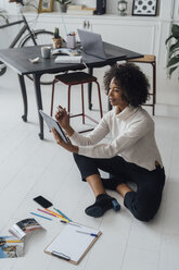 Disigner sitting on ground of her home office, using digital tablet - BOYF00915