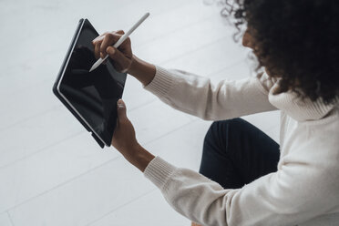 Disigner sitting on ground of her home office, using digital tablet - BOYF00916