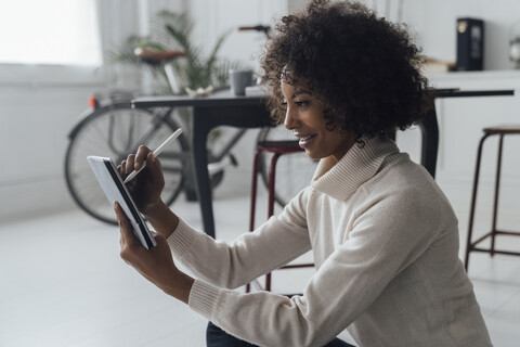 Die Absenderin sitzt auf dem Boden ihres Heimbüros und benutzt ein digitales Tablet, lizenzfreies Stockfoto