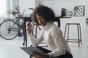 Disigner sitting on ground of her home office, using digital tablet - BOYF00918