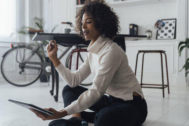 Disigner sitting on ground of her home office, using digital tablet - BOYF00919