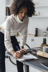 Freelancer standing at hert desk, using calculater, taking notes - BOYF00929