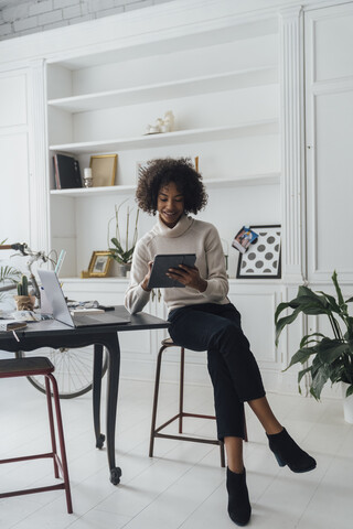 Mittlere erwachsene Freiberuflerin, die an ihrem Schreibtisch sitzt und mit Laptop und digitalem Tablet arbeitet, lizenzfreies Stockfoto