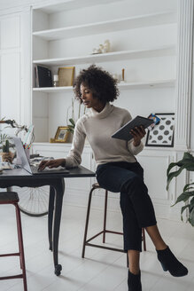 Mid adult freelancer sitting at her desk, working with laptop and digital tablet - BOYF00932