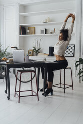 Mittlere erwachsene Frau sitzt in ihrem Büro zu Hause, lächelt und streckt sich - BOYF00938