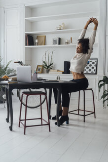 Mid adult woman sitting in her home office, smiling and stretching - BOYF00938