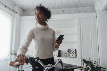 Mid adult woman leaving her home office, pushing bicycle, using smartphone - BOYF00945