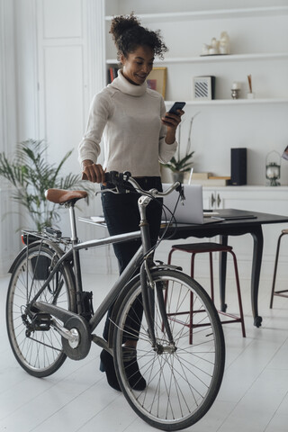 Mid adult woman leaving her home office, pushing bicycle, using smartphone stock photo