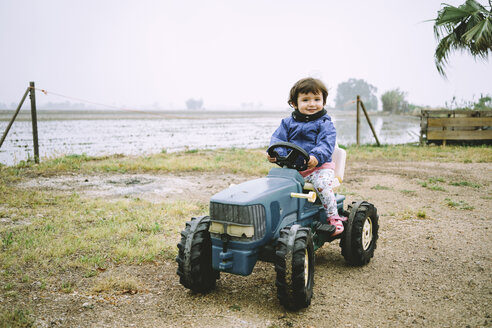 Ein kleines Mädchen fährt einen Spielzeugtraktor neben den Reisfeldern - GEMF02500