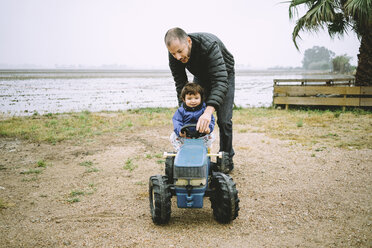Vater hilft einem kleinen Mädchen, einen Spielzeugtraktor neben den Reisfeldern zu fahren - GEMF02502
