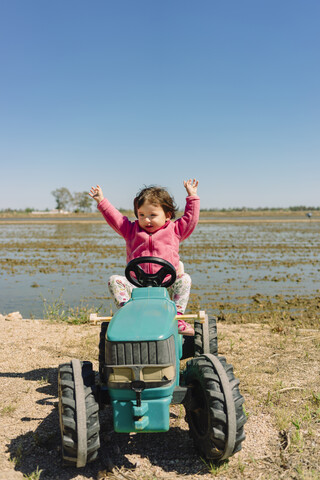 Ein kleines Mädchen fährt einen Spielzeugtraktor neben den Reisfeldern, lizenzfreies Stockfoto