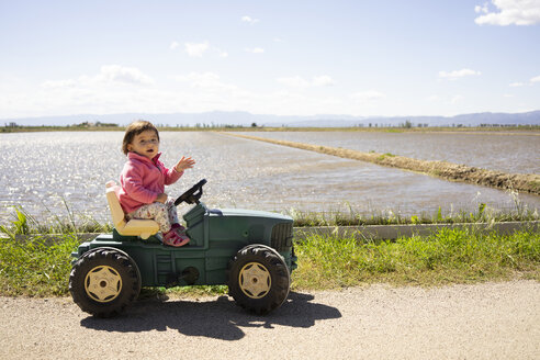 Ein kleines Mädchen fährt einen Spielzeugtraktor neben den Reisfeldern - GEMF02514