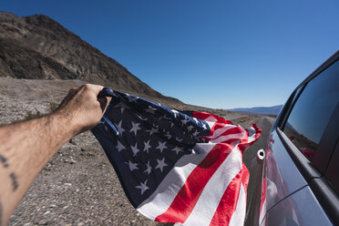 USA, Kalifornien, Death Valley, Männerhand hält amerikanische Flagge neben Auto - KKAF02955