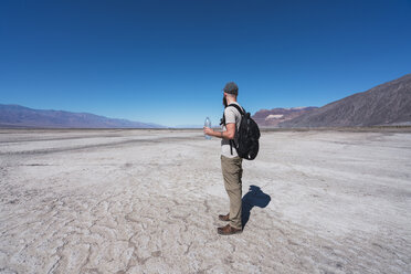 USA, Kalifornien, Death Valley, Mann mit Rucksack und Wasserflasche steht in der Wüste und schaut in die Ferne - KKAF02959