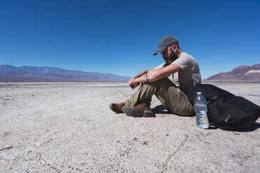 USA, Kalifornien, Death Valley, Mann sitzt auf dem Boden in der Wüste und ruht sich aus - KKAF02962