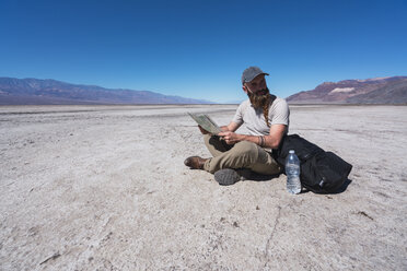 USA, Kalifornien, Death Valley, Mann sitzt auf dem Boden in der Wüste mit Karte und ruht sich aus - KKAF02963