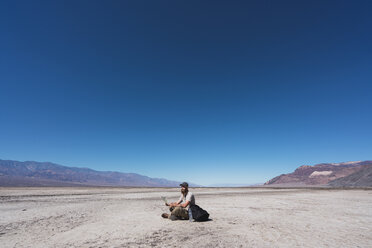 USA, California, Death Valley, man with map sitting on ground in the desert having a rest - KKAF02964
