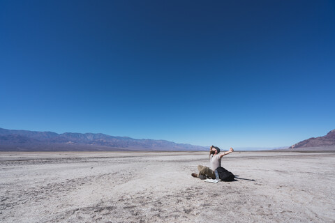 USA, Kalifornien, Death Valley, Mann sitzt auf dem Boden in der Wüste, lizenzfreies Stockfoto