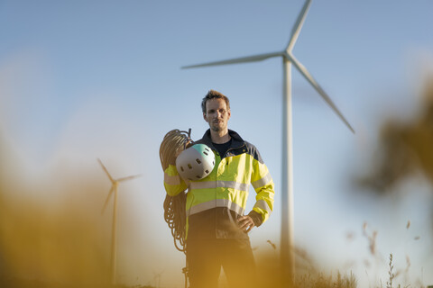 Technician standing in a field at a wind farm with climbing equipment stock photo