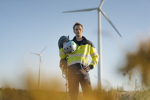 Technician standing in a field at a wind farm with climbing equipment stock photo