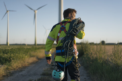 Techniker auf einem Feldweg in einem Windpark mit Kletterausrüstung, lizenzfreies Stockfoto