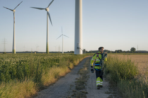 Techniker auf einem Feldweg in einem Windpark mit Kletterausrüstung - GUSF01339