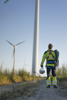 Technician standing on field path at a wind farm with climbing equipment - GUSF01340