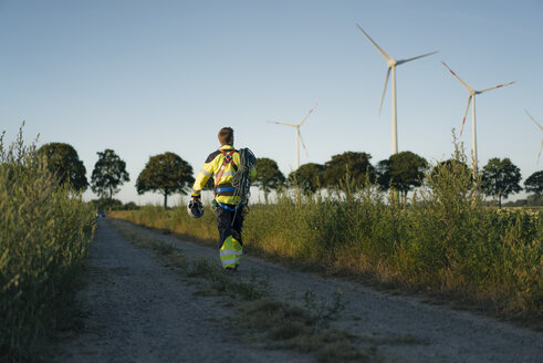 Techniker auf einem Feldweg in einem Windpark mit Kletterausrüstung - GUSF01344