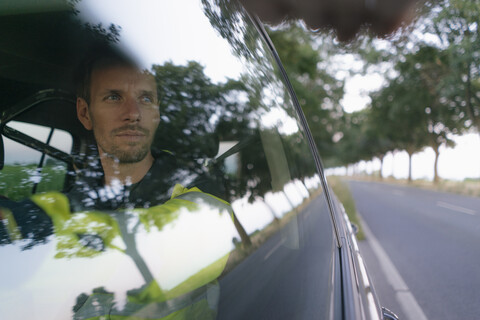 Mann in Arbeitsschutzkleidung in einem Auto an einer Landstraße, lizenzfreies Stockfoto