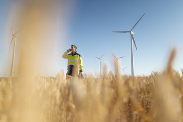 Ingenieur steht auf einem Feld in einem Windpark und spricht mit seinem Handy - GUSF01368