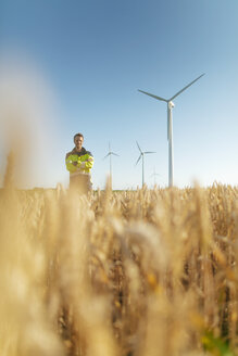 Porträt eines lächelnden Ingenieurs, der auf einem Feld in einem Windpark steht - GUSF01373