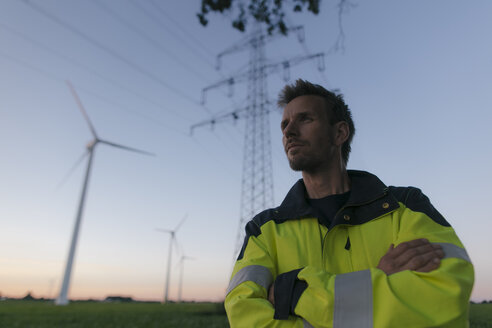 Porträt eines Ingenieurs neben einem Windpark und einem Strommast - GUSF01386