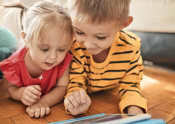 Bruder und kleine Schwester liegen zu Hause auf dem Boden und benutzen ein digitales Tablet - ZEDF01769