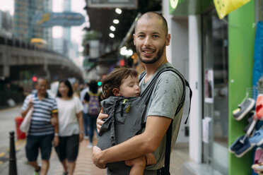 China, Hongkong, Porträt eines reisenden Vaters mit einem kleinen Mädchen, das in einer Babytrage schläft - GEMF02518