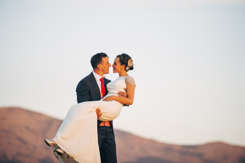 Bräutigam trägt Braut in ländlicher Landschaft, lizenzfreies Stockfoto