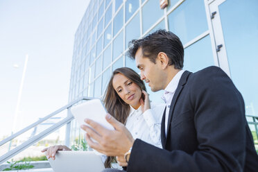 Businesswoman and businessman working with tablet and laptop outside office building - KIJF02093