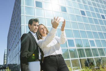 Smiling businesswoman and businessman taking a selfie outside office building - KIJF02099